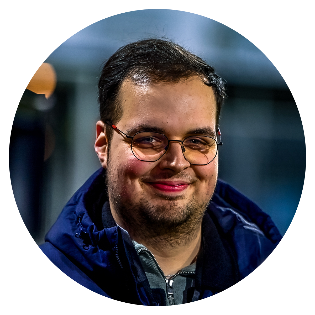 Portret van Wouter Bos, een jonge man met een glimlach, gekleed in een donkere jas en met een ronde bril.